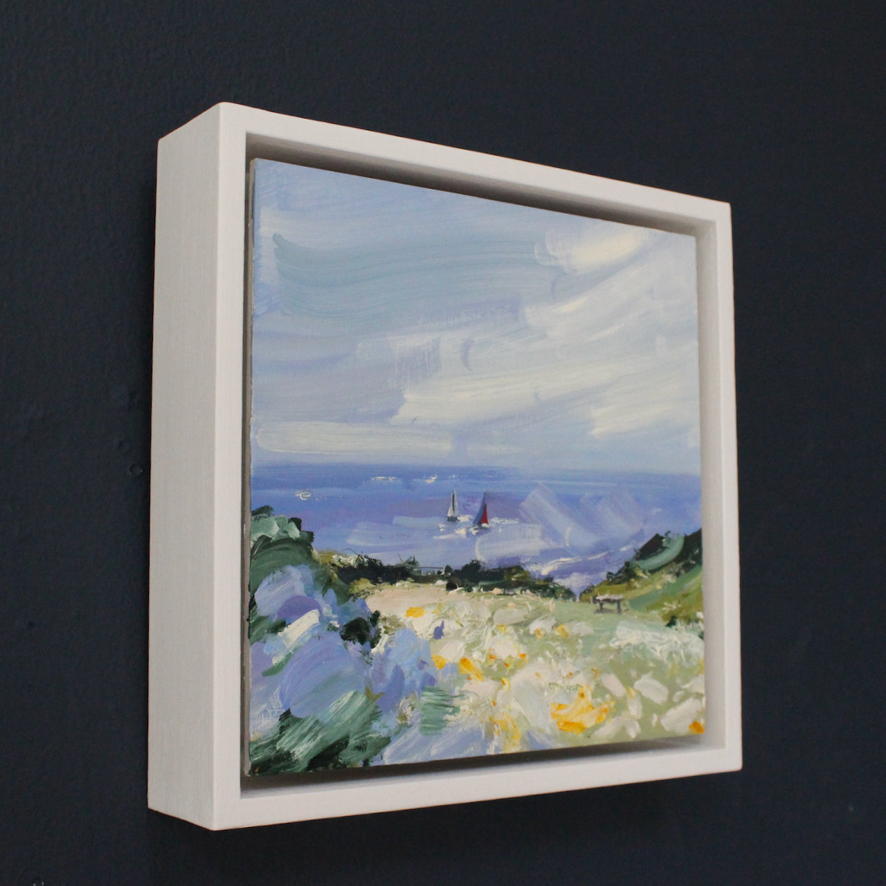 a small framed Seascape by artist Jill Hudson of boats sailing in the background and coastal landscape in foreground.