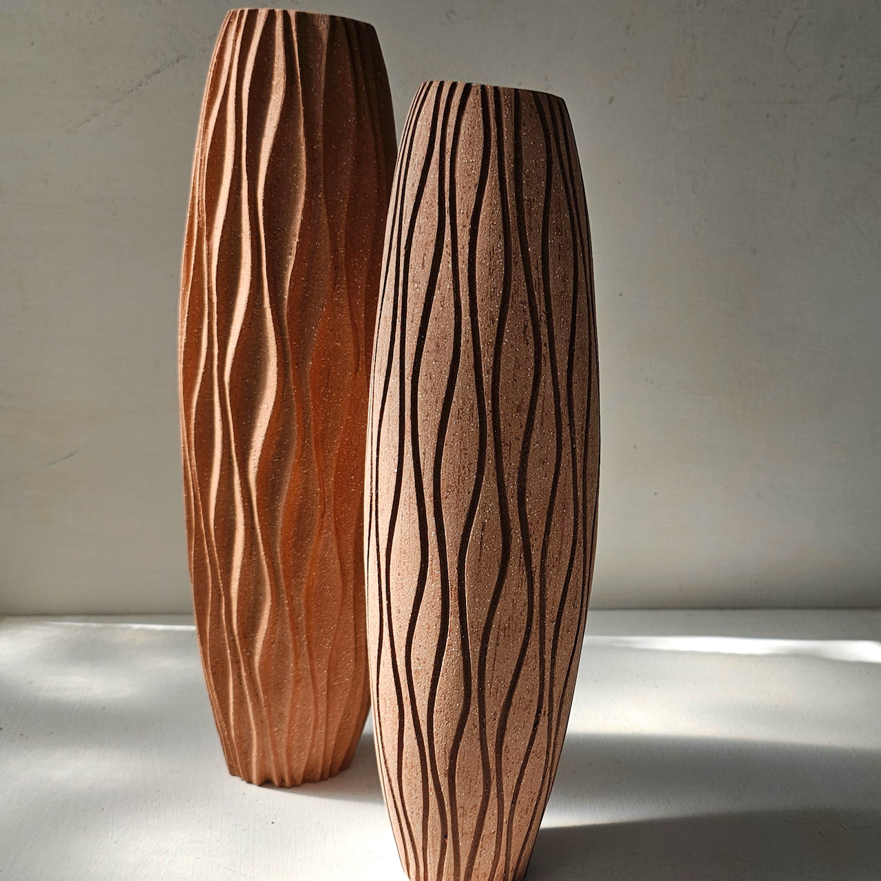 Mid-red stoneware kelp detailed vase alongside mid-red stoneware with inlaid dark red vessels by artist Michele Bianco