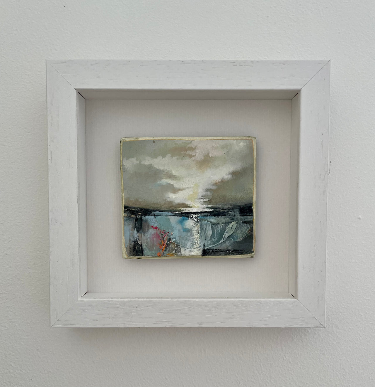 a small framed painting by artist Julie Ellis of a dark brooding sky over a blue, black and pink sea 