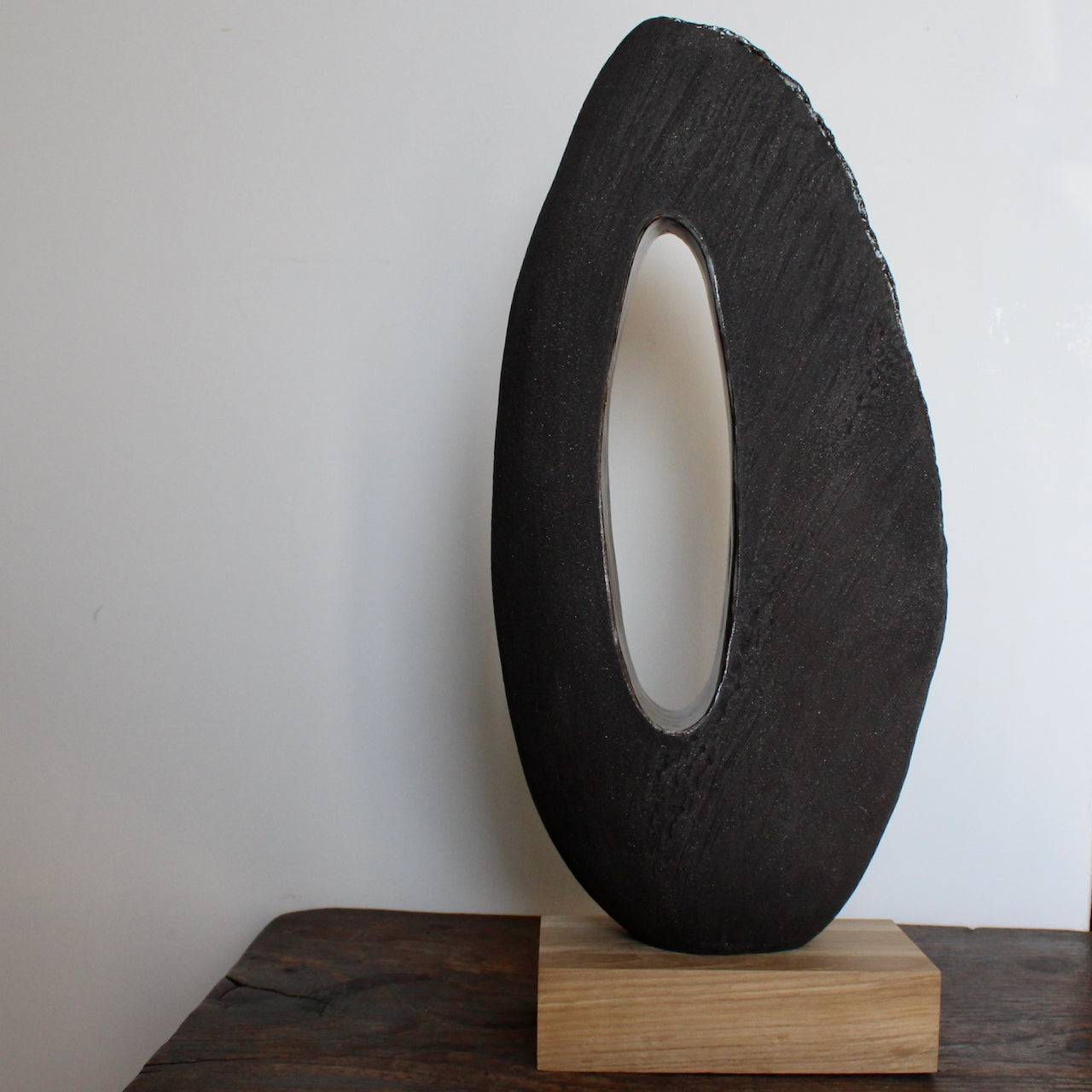 Brown oval shaped sculpture with hollow centre on an oak stand by Cornish artist Anthea Bowen