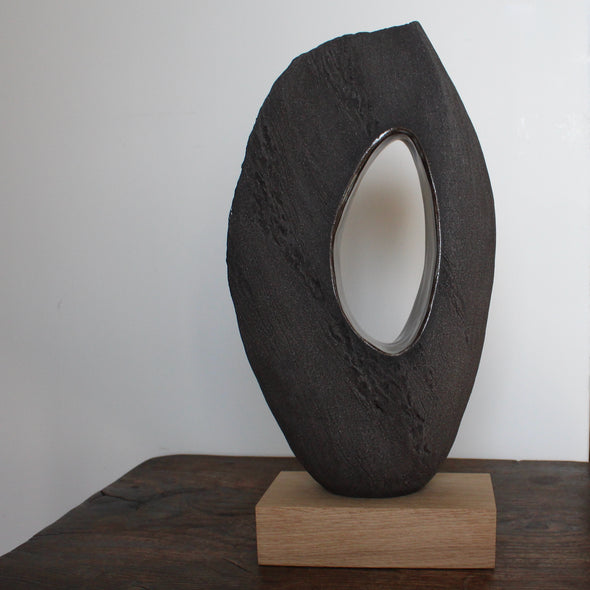 Oval brown sculpture with hollow centre on an oak stand by Anthea Bowen, Cornish artist