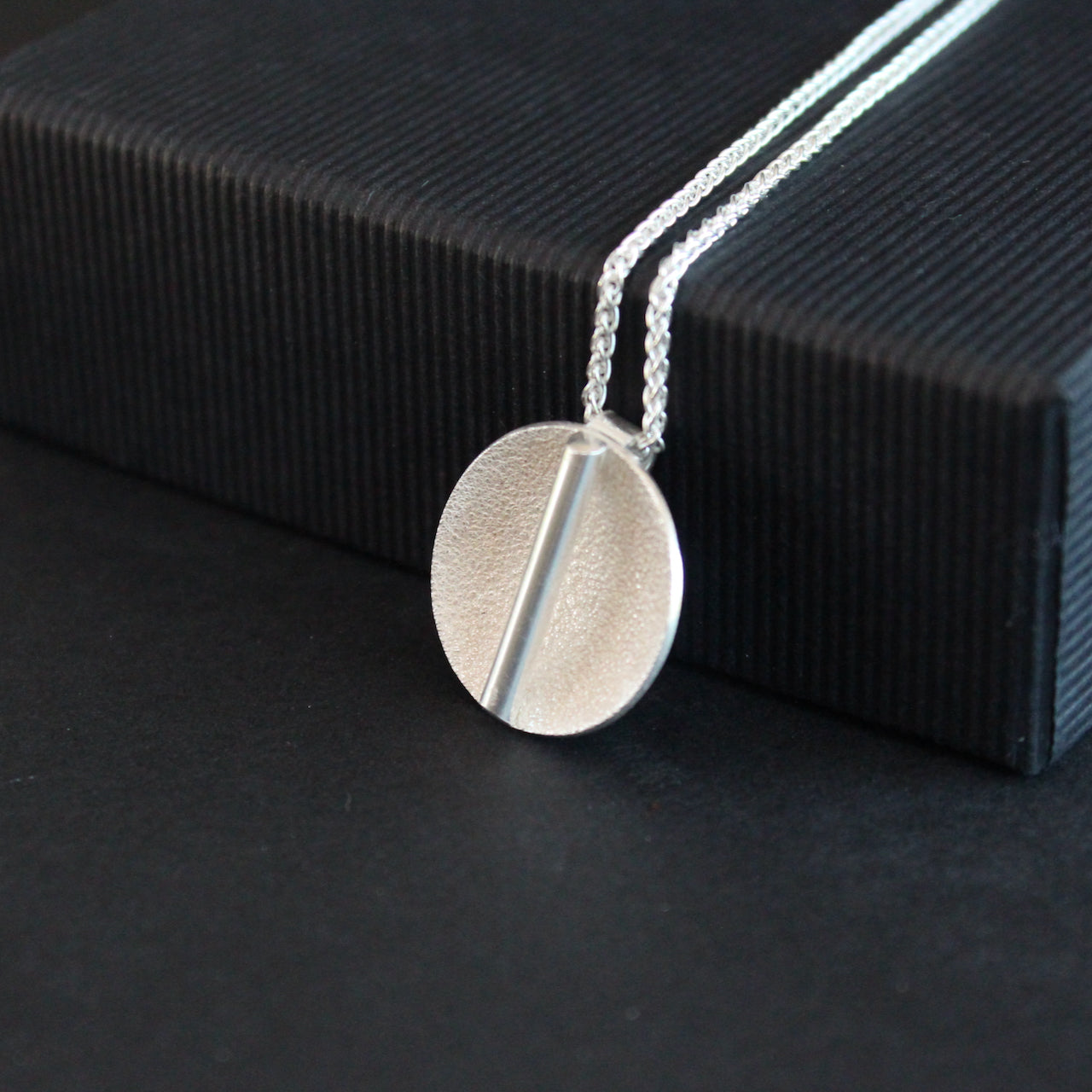 a textured silver disc pendant with a central bar by Uk jeweller Beverly Bartlett