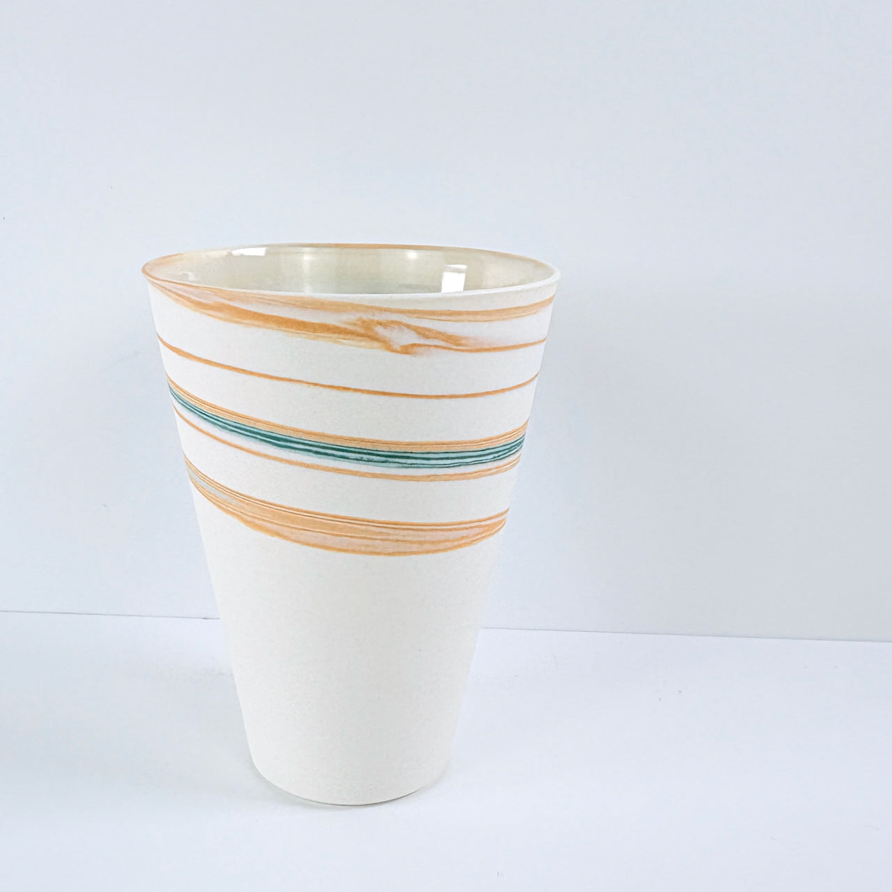 Ceramic cup with orange and blue stripes on a white background by Deborah Greenwood