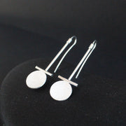 a pair of Beverly Bartlett silver drop earrings with a textured silver disc under a silver horizontal bar