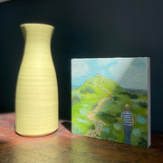 A figure in a stripy blue and white top walking towards a building on top of a hill with a footpath leading to the building by UK artist Siobhan Purdy.