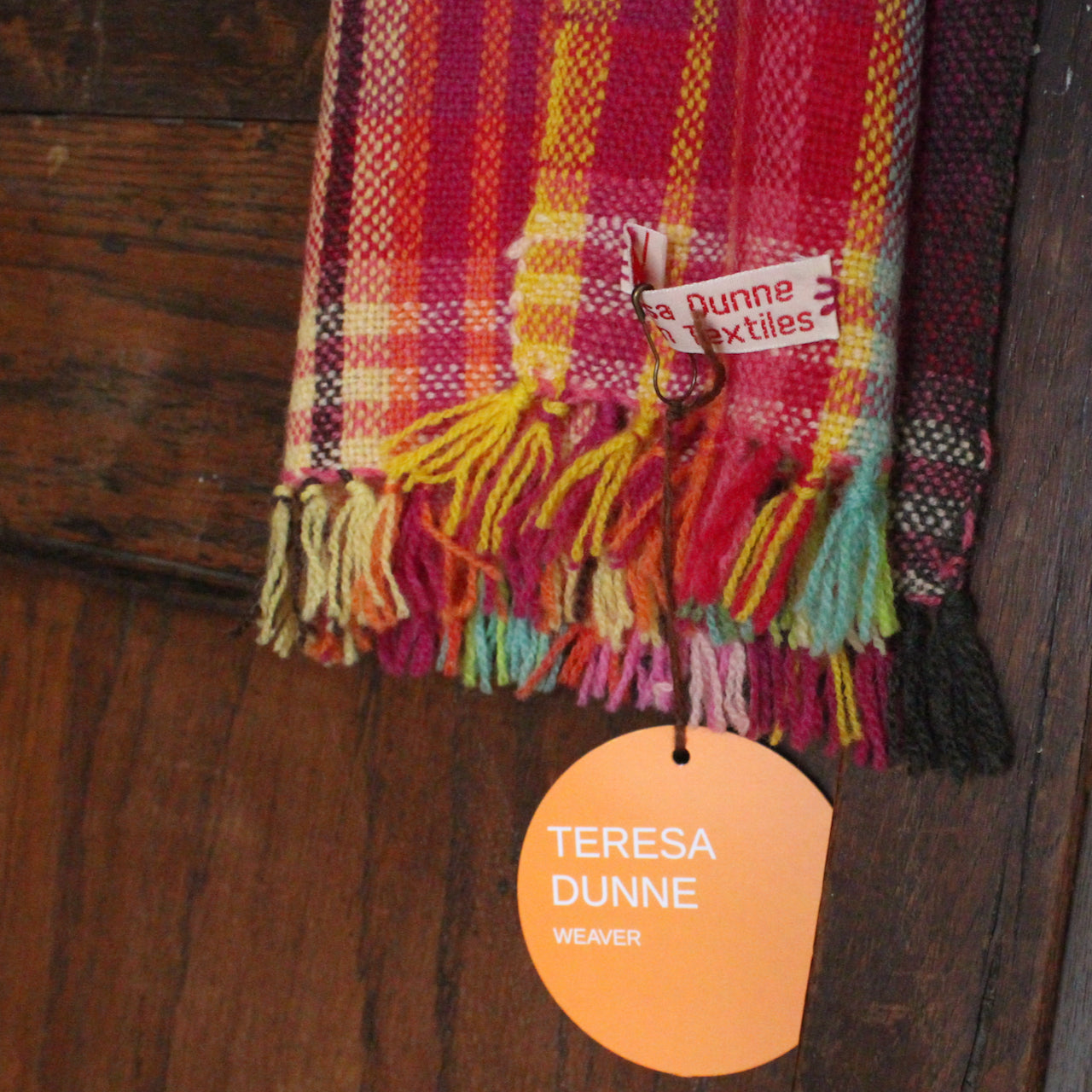 close up detail of a handwoven woollen scarf by Teresa Dunne Cornish weaver in red, green, orange and yellow