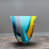tall and gently curved multi-coloured glass vase on a wooden table it is made by Ruth Shelley 