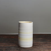 white ceramic cylinder vase with pale yellow stripes on a wooden table 
