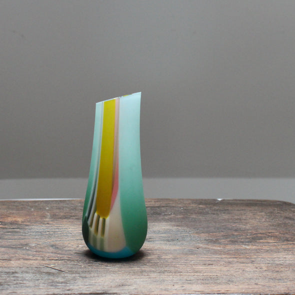 a small glass vase in green pinks and yellows with an angled top made by glass artist Ruth Shelley.