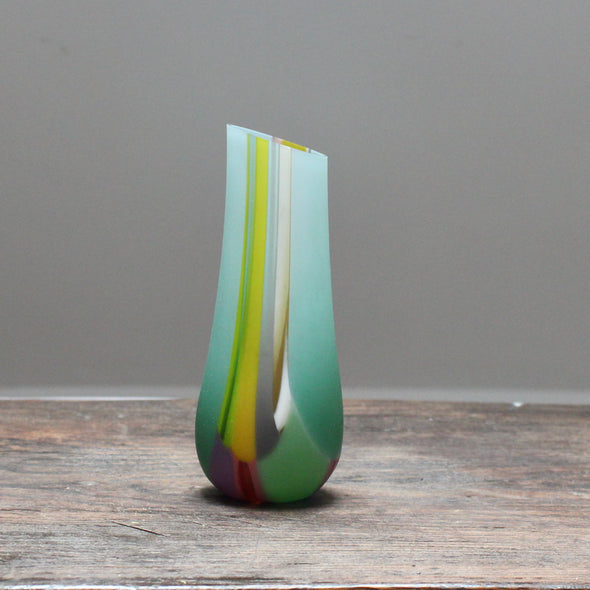 small glass vase in green pinks and yellows with an angled top made by glass artist Ruth Shelley
