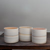 three ceramic pots with pale pink interiors and pastel stripes on the outside 