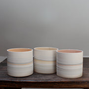 a set of three small ceramic pots with pale interiors and pastel stripes on the outside. 