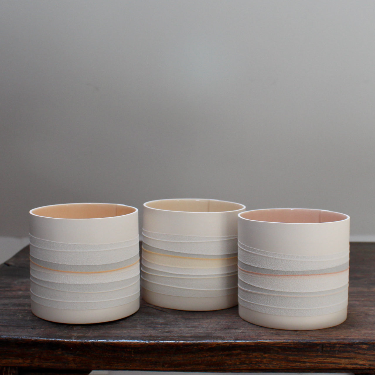 a set of three small ceramic pots with pale interiors and pastel stripes on the outside. 