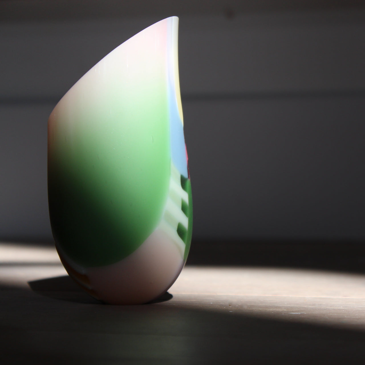 a small glass vase in pink, mauve and pale green stripes with an angled rim by glass artist Ruth Shelley