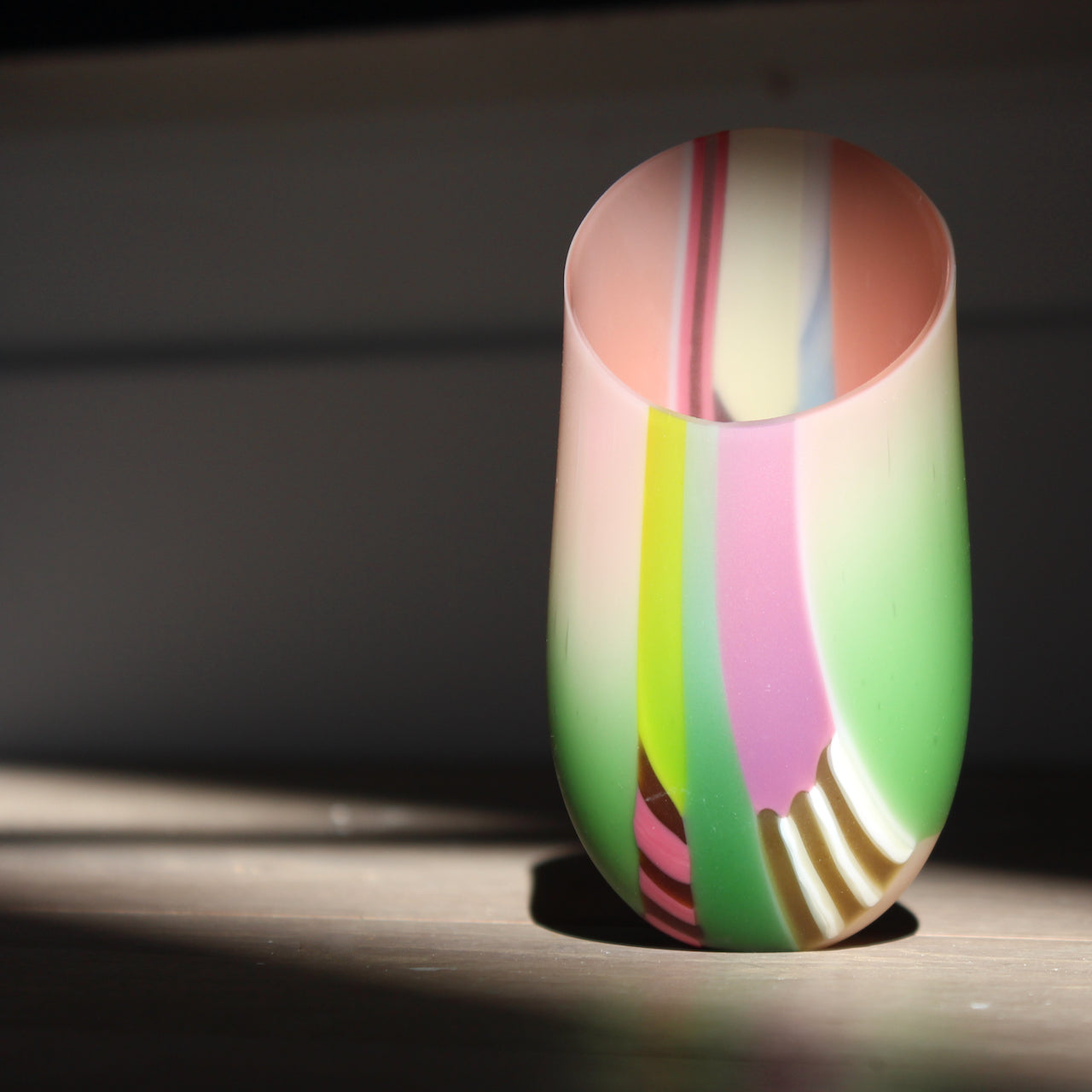 small glass vase in pink, mauve and pale green stripes with an angled rim by UK glass artist Ruth Shelley.