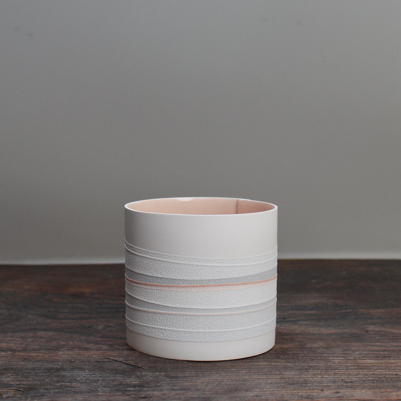 a white ceramic pot with a pale pink interior and pink and grey stripes on the outside sitting on a wooden table.