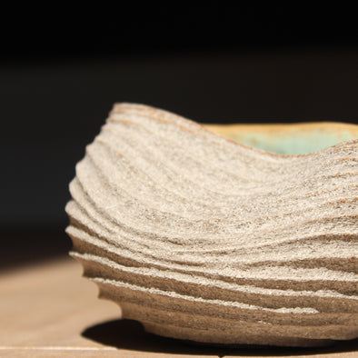 a stoneware bowl which has been hand carved to create a slumped and ribbed effect on the exterior with a pale green glaze inside it was made by UK ceramic artist Michele Bianco 