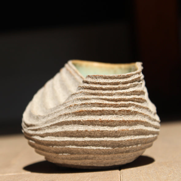 stoneware bowl which has been hand carved to create a slumped and ribbed effect on the exterior with a pale green glaze inside it was made by UK ceramic artist Michele Bianco.