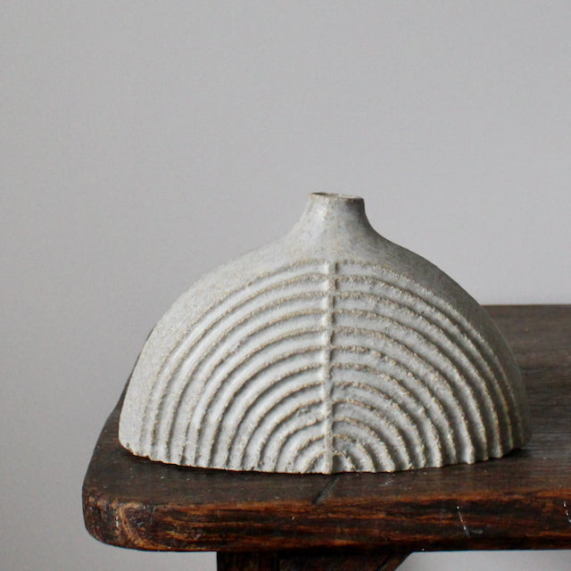 a rounded and carved pale grey stoneware bottle by Michele Bianco on a dark wood table.