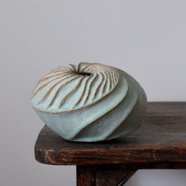 A round and carved pale green ceramic vessel by Michele Bianco photographed on a dark wood table