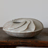 A round and carved ceramic vessel by Michele Bianco photographed on a dark wood table 