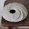 The top view of round and carved ceramic vessel by Michele Bianco photographed on a dark wood table.