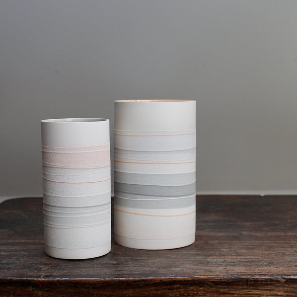 two white ceramic vases with pale orange and grey stripes on a wooden table. 