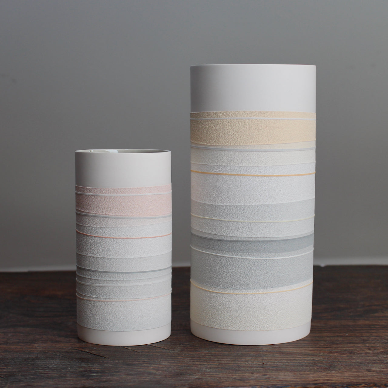 two white ceramic cylinder vases with pale orange and grey stripes.