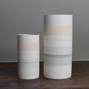 two white ceramic cylinder vases with pale coloured stripes on a wooden table.