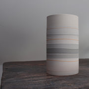 a white ceramic cylinder vase with pale orange and grey stripes.