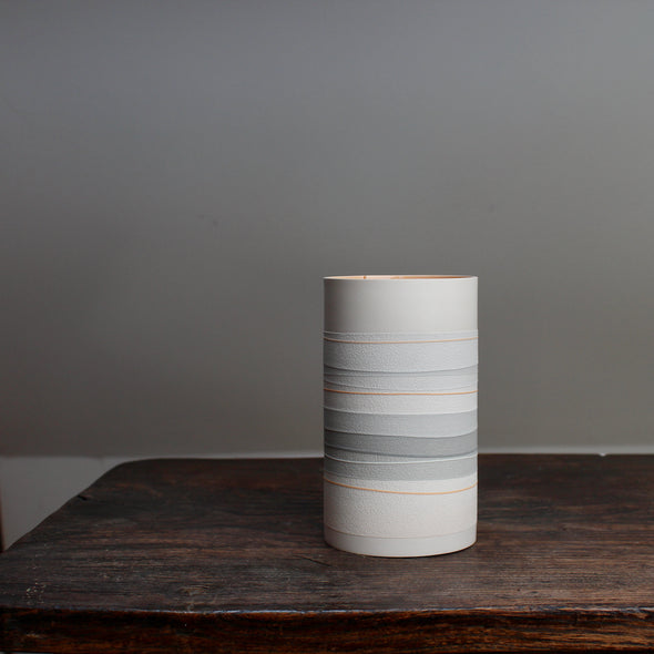 a white ceramic vase with pale orange and grey stripes on a table.