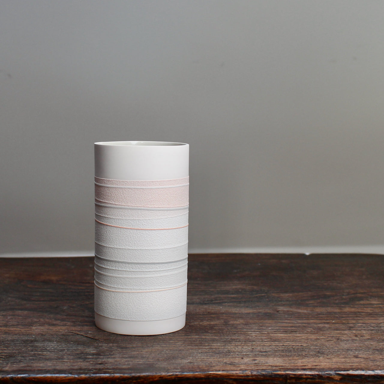 A ceramic cylinder with orange and pale grey stripes 