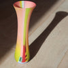 a tall and narrow glass vase in pink, yellow and lime green stripes by UK glass artist Ruth Shelley.