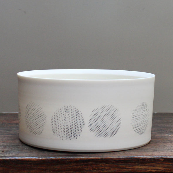 a white porcelain serving dish decorated with abstract black circles.