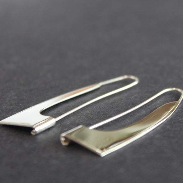 a pair of curved silver earrings in the shape of a sail