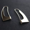 curved silver earrings in the shape of a sail photographed on a black background