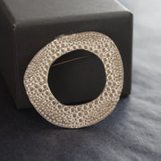 a textured silver round brooch with a hollow middle by jeweller Ann Bruford.