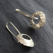 a pair of silver drop earrings with a hollow centre and a delicate pattern of circles by Ann Bruford 