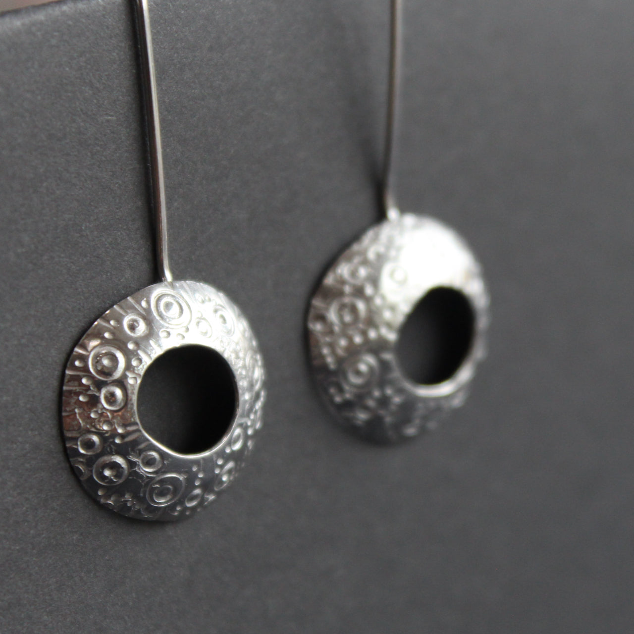 a pair of silver drop earrings with a hollow centre and a delicate pattern of circles by UK jeweller Ann Bruford