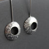 a pair of silver drop earrings with a hollow centre and a delicate pattern of circles by UK jeweller Ann Bruford 