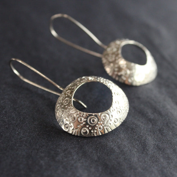a pair of large silver drop earrings by Ann Bruford with a hollow centre and a textured surface pattern