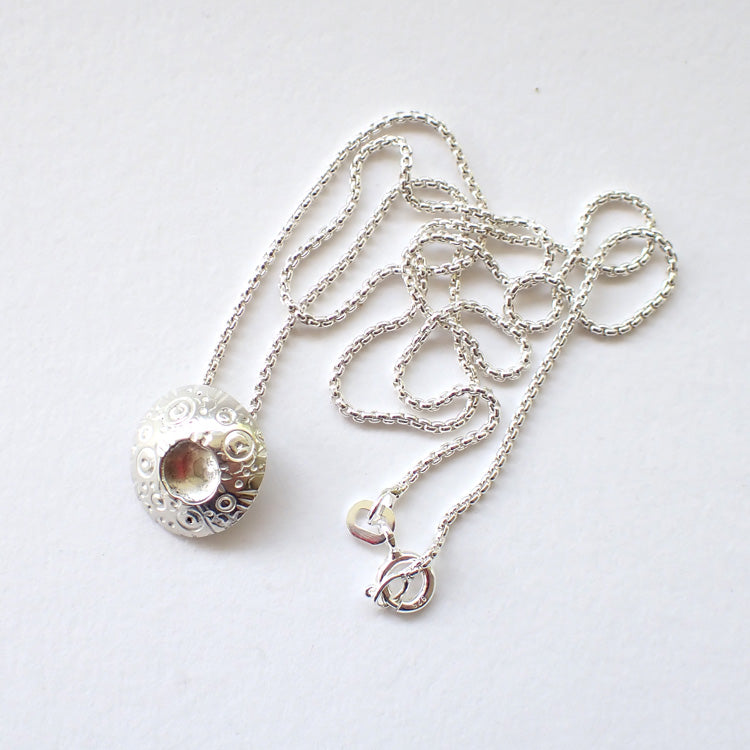 circular silver pendant with an indented middle and a textured surface design on a silver chain by Devon jewellery designer Ann Bruford