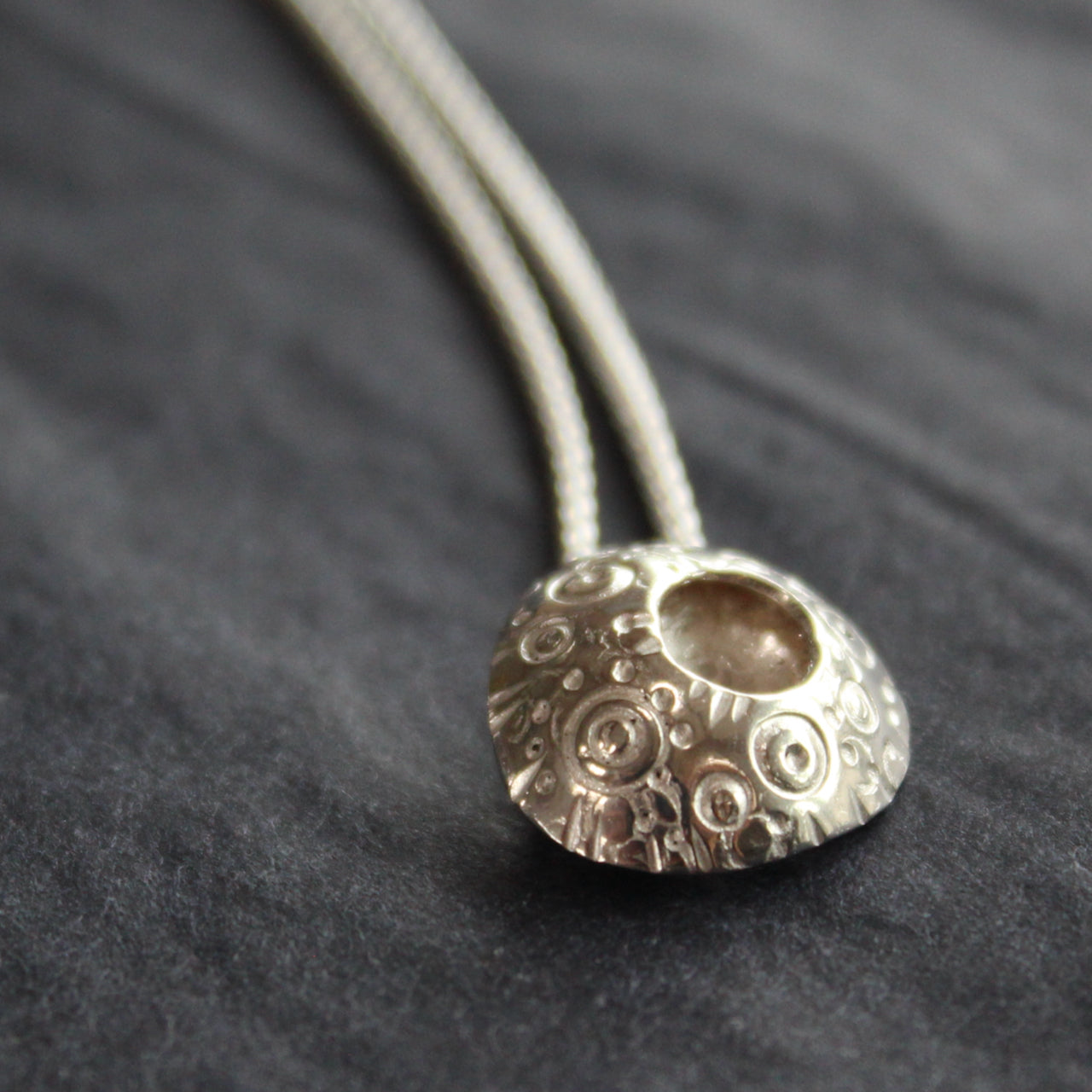 a circular silver pendant with an indented middle and a textured surface design on a silver chain by Devon jewellery designer Ann Bruford 