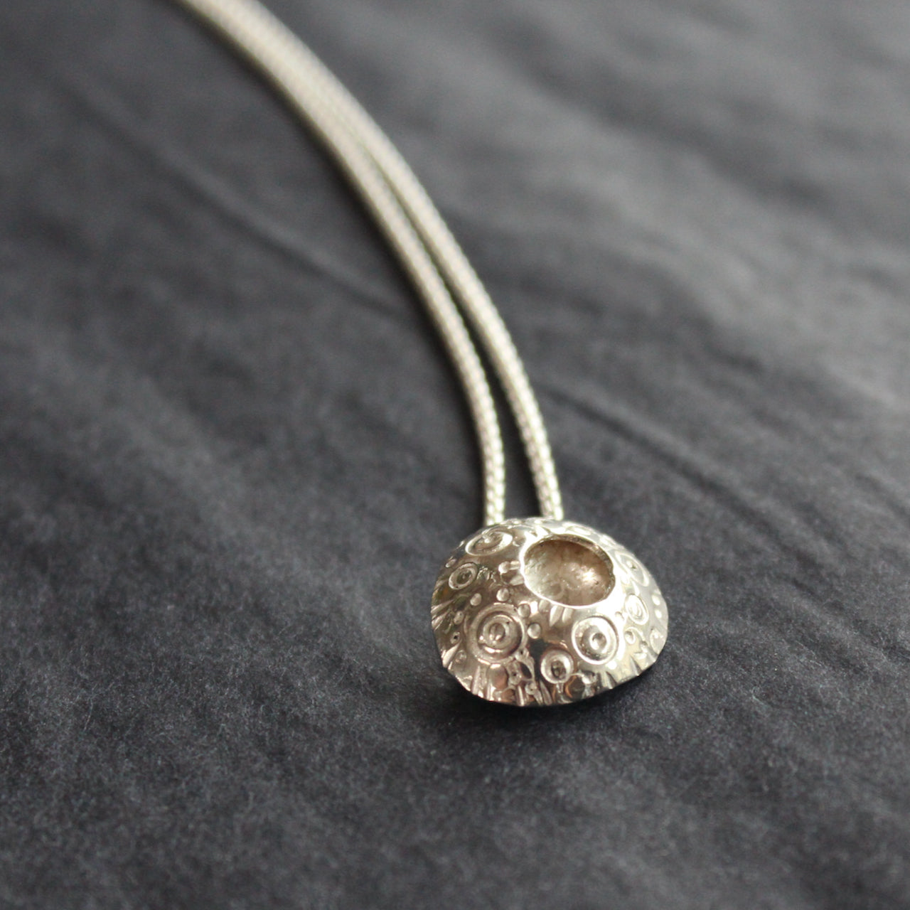 circular silver pendant with an indented middle and a textured surface design on a silver chain by Devon jeweller Ann Bruford 
