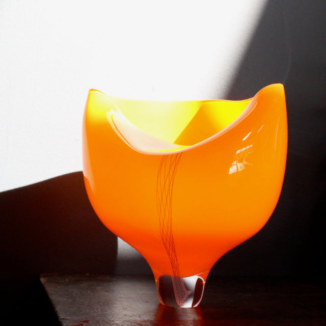 photographed in the sunlight, a orange coloured glass vessel with line detail to the front made by UK glass artist Benjamin Lintell.