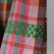 Close up of handwoven scarf with orange, pink and green hanging over a display rail 