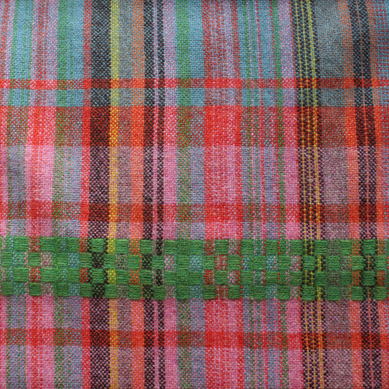 Close up of a handwoven scarf with orange, pink and green 