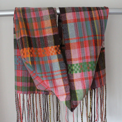 A Handwoven scarf with orange, pink and green hanging over a display rail 