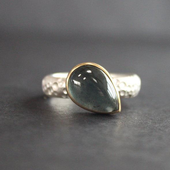 silver ring with teardrop shaped blue grey stone in gold setting by Carin Lindberg jewellery designer