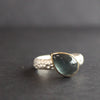 a silver ring with teardrop shaped blue grey stone in gold setting by Carin Lindberg jewellery designer.